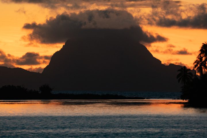 a sunset over a body of water with a mountain in the background
