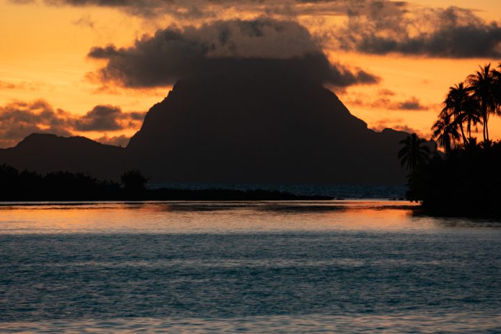 a sunset over a body of water with a mountain in the background
