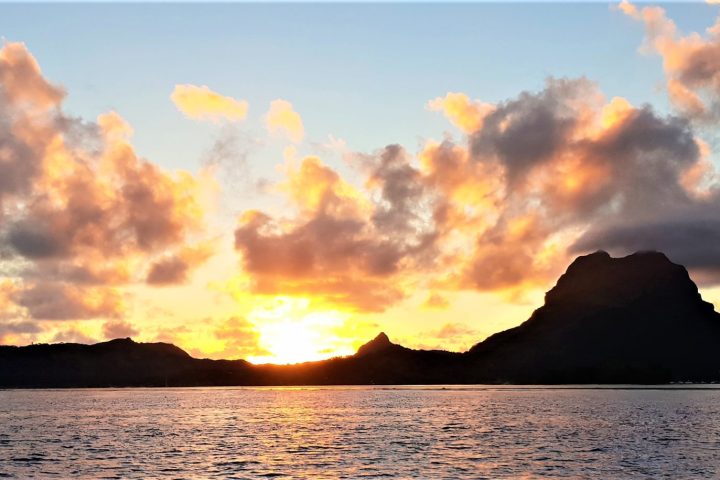 a sunset over a body of water with a mountain in the background